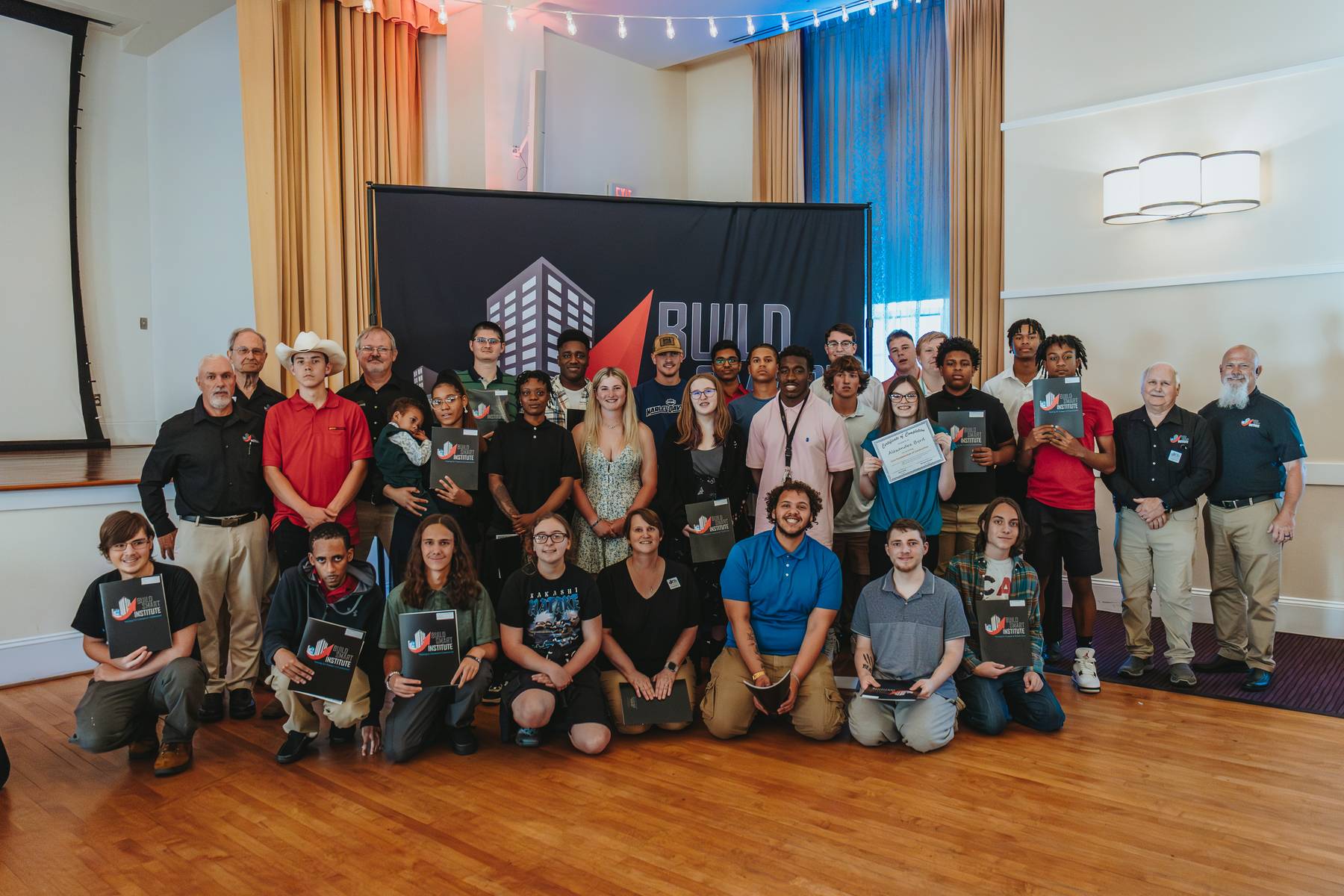 Photo of graduate group of 25-30 individuals in front of the Build Smart Institute Banner