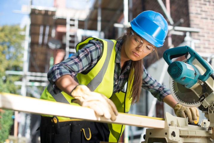 female carpenter cutting a board on a construction site