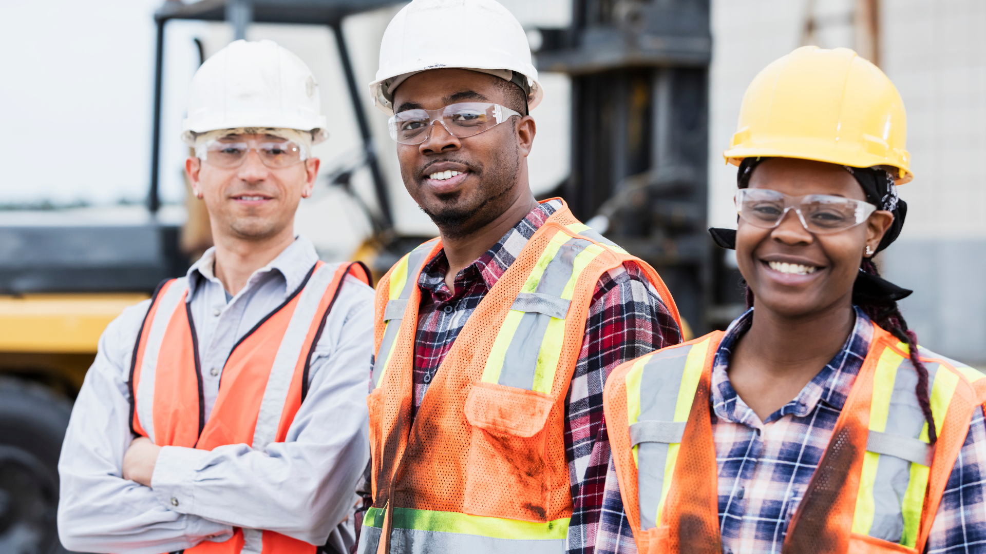 two male and one female construction workers smiling toward the camera while on a construction site.