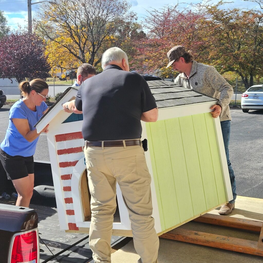 three people loading a small shed on a truck