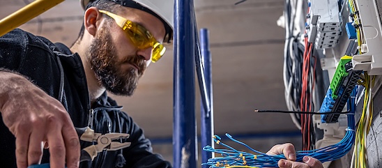 Electrician in a hard hat working in an electrical box and holding wire cutters