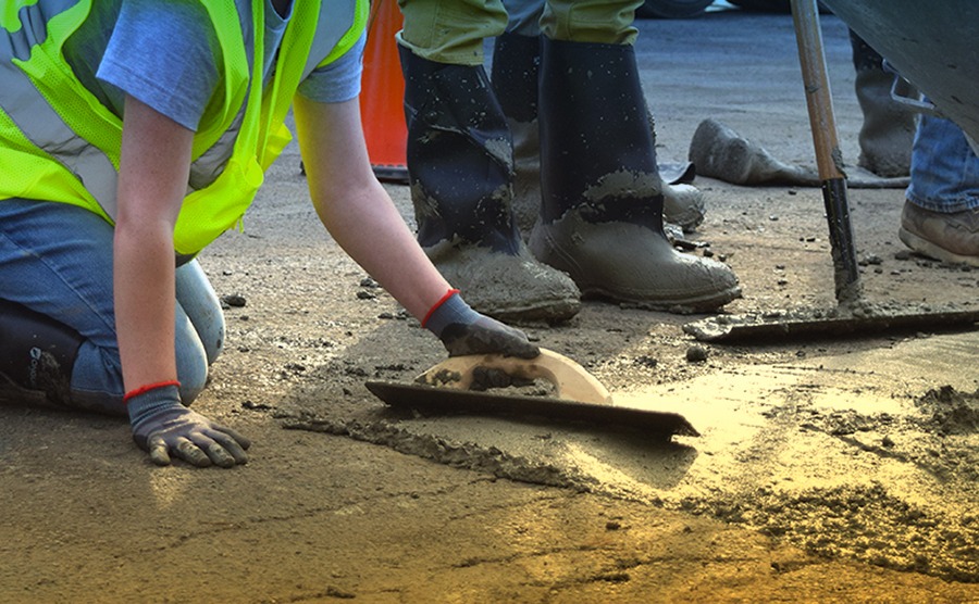 student on knees leveling concrete.